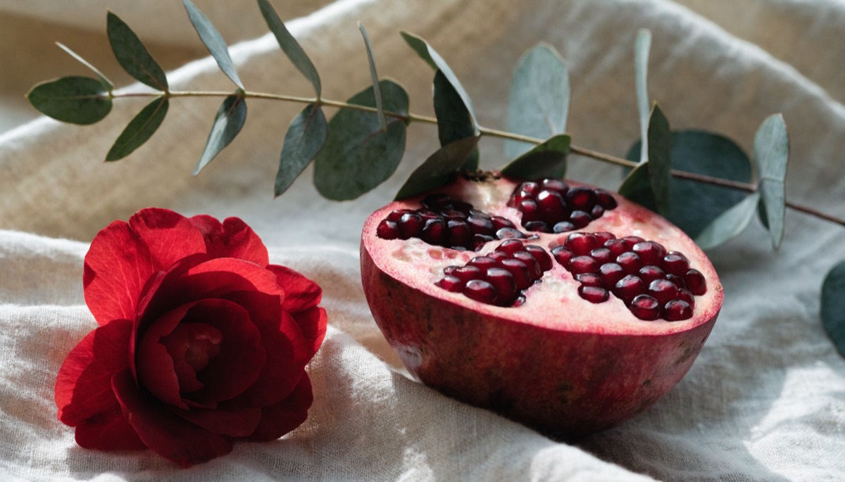 A halved pomegranate and red flower on cream linen